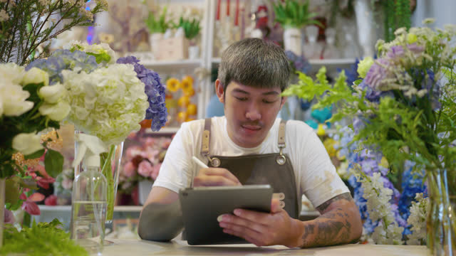 Asian owner men working with a digital tablet at the counter of flower shop.