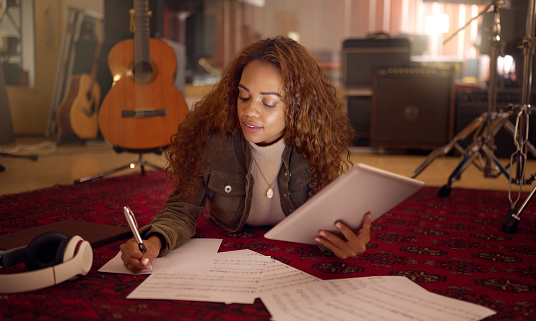 Musician, studio and woman writing lyrics for a song with paper and a digital tablet for composition. Creative, composer and female musical artist from Mexico working on a album, sound track or sound