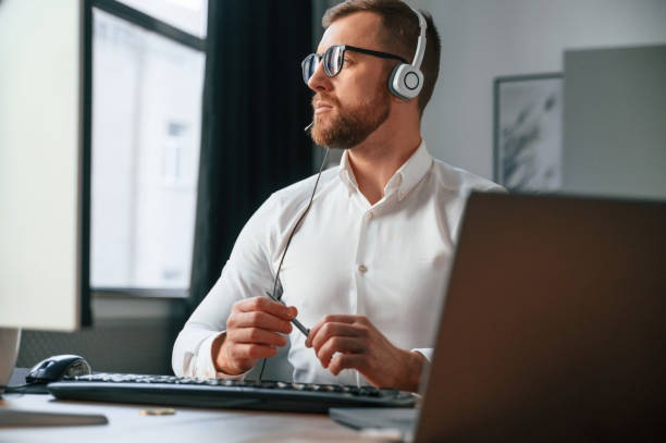 istock In headphones. Man in formal clothes is working in the modern office. Using computer 1478328006