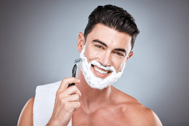 navaja, cara y hombre con crema de afeitar en estudio aislado sobre fondo gris. barba, toalla y retrato de modelo masculino feliz con producto facial, espuma o gel para afeitarse para bienestar y depilación. - male towel men human face fotografías e imágenes de stock