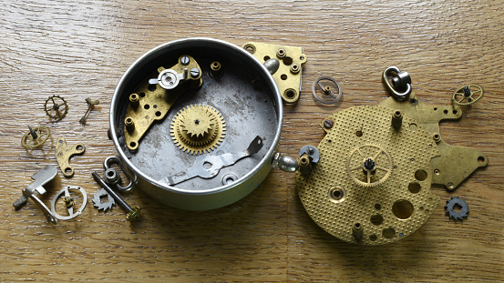 Still life with gear wheels and other elements of clock mechanism on the wooden desk
