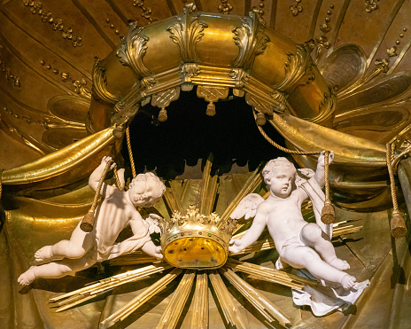Two white marble putti or child angels holding gilded crown under a baroque baldaquin inside of a 17th century side chapel of St Martin's Cathedral in Bratislava