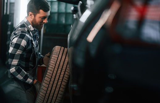 Changing the tire of the car. Man in uniform is working in the auto salon.