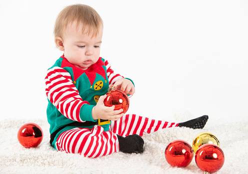 Stock studio photo with white background of a baby in elf costume grabbing christmas balls