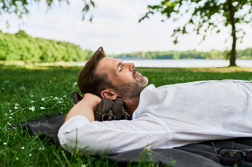 Side view of middleaged man lying down in park on grass taking a nap. Man sleeping in park