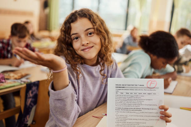 What can I do, I've got F grade on my test! Smiling schoolgirl feeling indifferent while showing her F grade on a test at elementary school and looking at camera. report card stock pictures, royalty-free photos & images