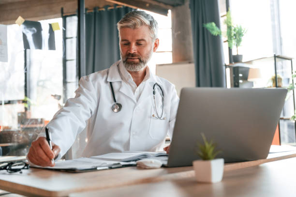 istock Writing information into document. Senior doctor in white coat is at work indoors 1478344673