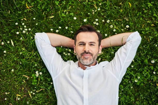 Handsome adult man lying down on grass with daisies stock photo