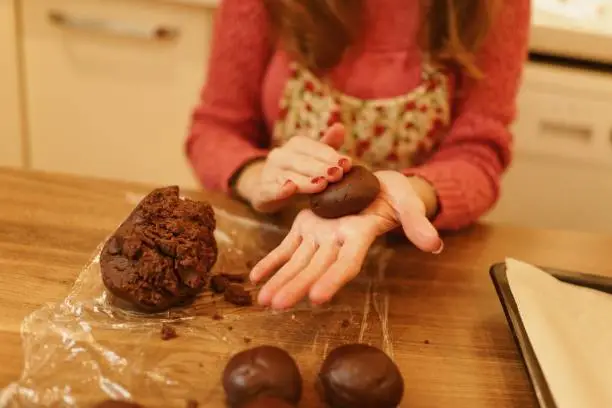 Close-up image of a woman shaping cookies with her hands in the kitchen, with only her hands visible.