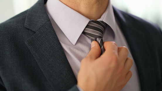 Businessman in suit straightening tie on shirt with hand closeup. Stylish elegant male look concept