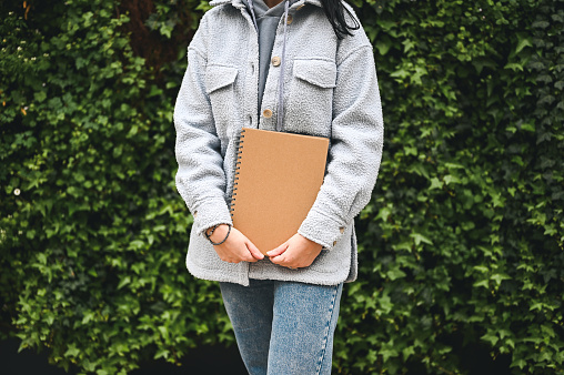 midsection of a mid adult woman with brochure in hands against a green plants outdoors.