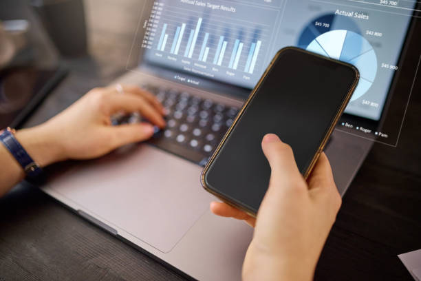 istock Hands, phone and laptop with hologram in analytics for chart, graph or marketing statistics. Hand of analyst checking 3D digital data for corporate or company sales on computer with smartphone mockup 1478354929
