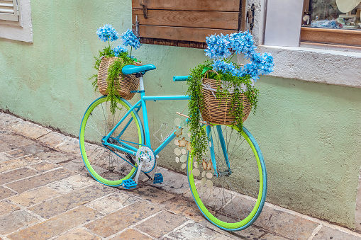 A bright bicycle decorated with wicker baskets of flowers stands on the street in the Old Town of Budva, Montenegro. Vintage decor near an ancient building in Stari Grad, outdoors