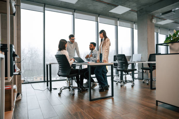 istock Against big windows by the table. Four people are working in the office together 1478357177