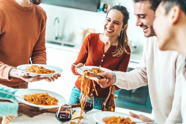 Happy group of friends eating pasta at home dinner party - Cheerful young people having lunch break together - Life style concept with guys and girls celebrating thanksgiving - Bright filter stock photo