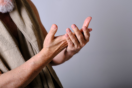 lateral view of the hands of an aged white man taking care of himself in a white background studio
