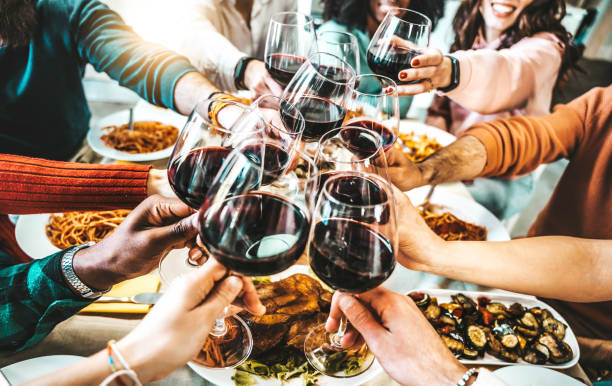 Happy friends toasting red wine glasses at dinner party - Group of people having lunch break at bar restaurant - Life style concept with guys and girls hanging out together - Food and beverage stock photo