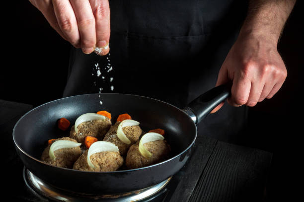 istock Cooking cutlets on grill pan by chef or cook hands on black background for copy space text restaurant menu. The chef adds salt 1478364505