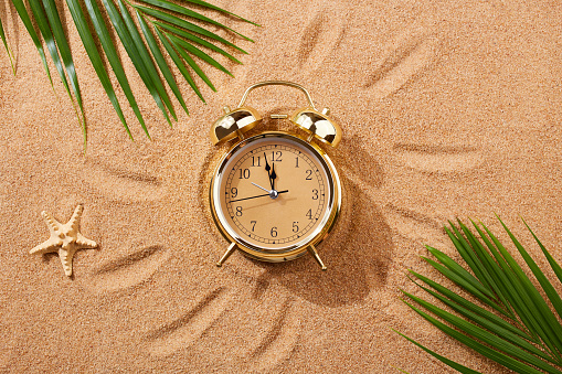 istock Alarm clock on a sandy beach. Noon, 12 p.m. A dangerous time for tanning and being in the sun.Sand texture, natural background. 1478368452