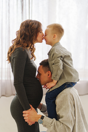 a loving and gentle family. pregnant mom, son sits on dad's shoulders and everyone kisses. the concept of family happiness. medical services for the whole family, family doctor.