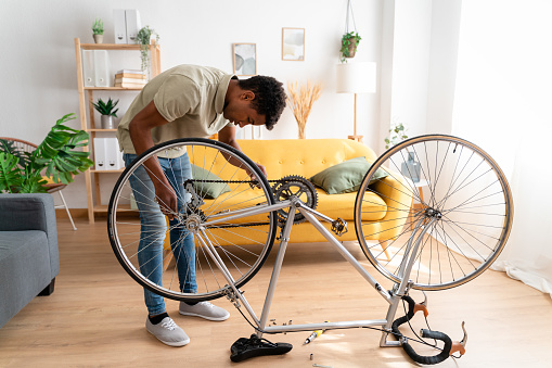 Side view of African American male in casual clothes sitting on floor near bicycle and looking at each other