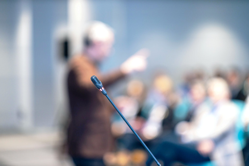 Microphone in focus, blurred speaker and audience at workshop, training, business conference or presentation