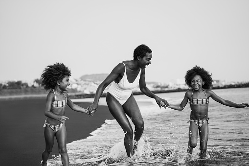 African sisters twins running on the beach with smiling mother - Focus on mom face - Black and white editing