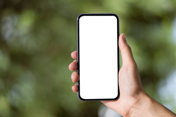 Man holding smartphone with blank screen, close-up of hands. Space for text and blur inside abstract green background with natural bokeh.