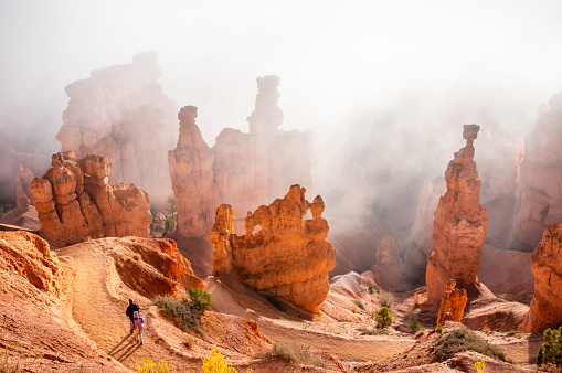 People trekking the Navajo loop trail in Bryce Canyon National Park at sunrise with some clouds and fog. Utah, USA