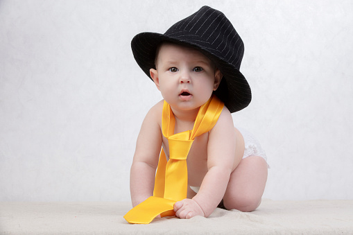 Smiling kid in a retro hat and tie on a white background. Funny six month old baby in elegant clothes.