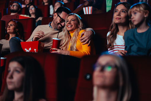 Young adult romantic lovers are in a movie theater enjoying some time together and watching a movie.