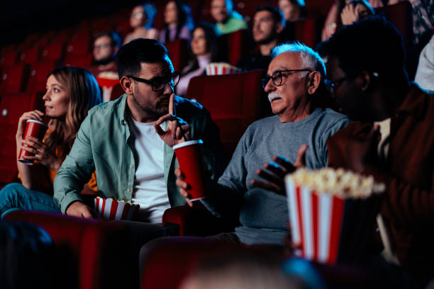 istock Man gesturing silence in movie theater. 1478374866