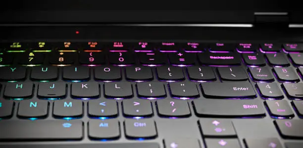 A closeup look of a black keyboard with backlit keys in different colours