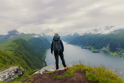 A male backpacker contemplating a view of beautiful bay of sea with green mountain peaks of Western Norway, Scandinavia