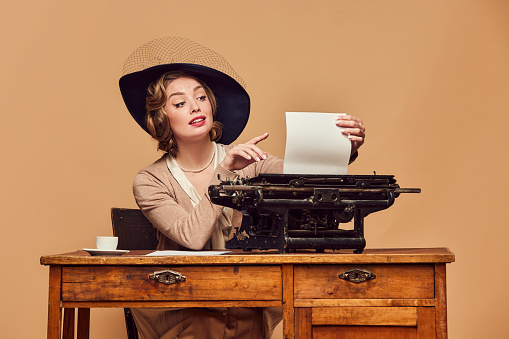 Surprise, wonder. Surprised beautiful woman writer wearing retro clothes sitting at typewriter with astonished face. Concept poems, novel, emotions, beauty, fashion, retro style, vintage, 60s