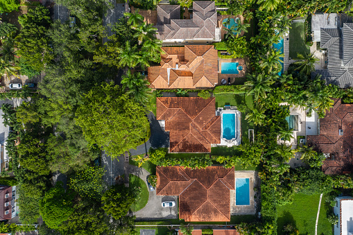 Aerial drone shot of suburb in Coral Gables city with large tropical greenery around, modern houses with elegance and style, summer weather, blue sky