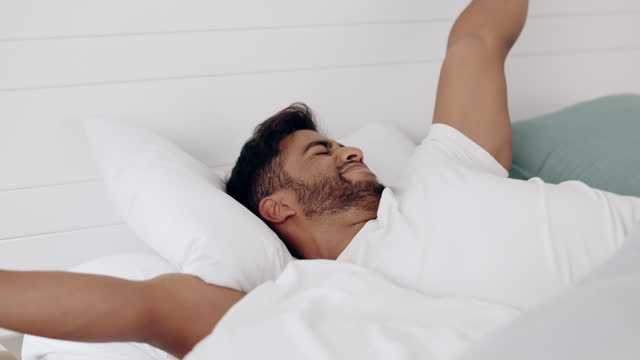 Wake up, stretching and morning with a man in bed to relax alone in his home over the weekend. Sleeping, lazy and lifestyle with a handsome young male awake after being asleep in his house for rest