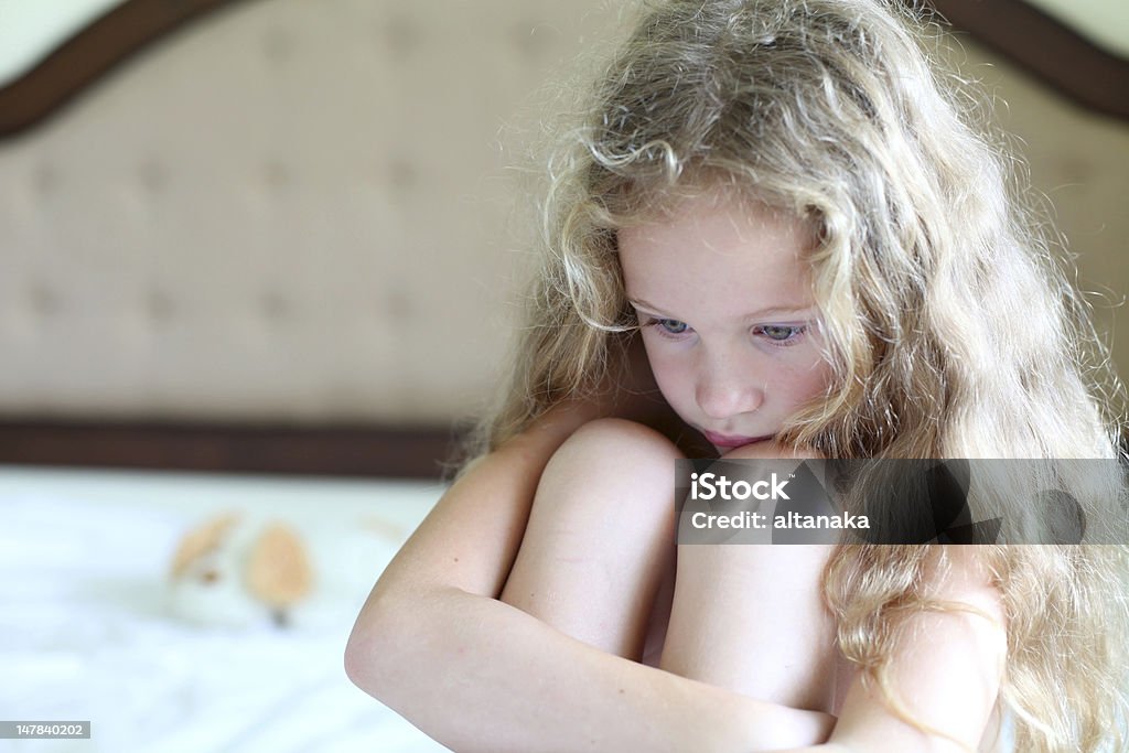 Photograph of sad young blonde girl a sad child sits on the bed Assistance Stock Photo