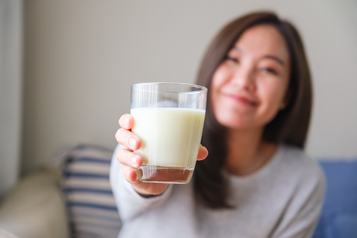 Blurred image of a young woman holding and showing a glass of fresh milk