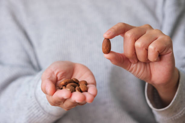 изображение крупным планом рук, держащих и показывающих миндаль - people snack almond brown стоковые фото и изображения