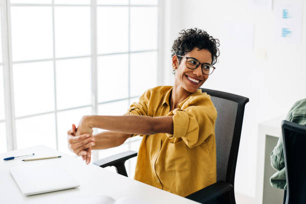 Business woman stretching her hands as she takes a break in the office Business woman stretching her hands as she takes a break in the office. Happy female professional sitting at her desk in an accounting firm. stretching stock pictures, royalty-free photos & images