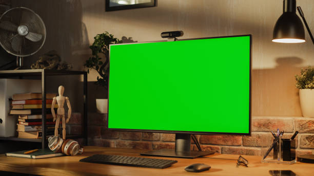 istock Computer Monitor with Green Screen Standing on a Wooden Desk with Height Adjustable Function. Chroma Key Display at Home in Modern Living Room or Creative Loft Office with Brick Wall 1478407563