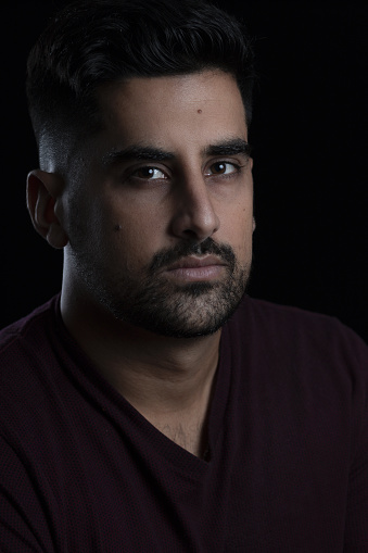 A closeup vertical portrait of a mature serious Hispanic man isolated on a black background