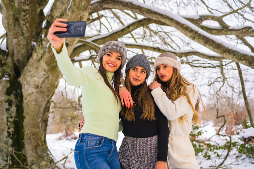 Three female friends taking a selfie under a tree in winter