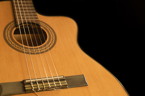 Partial view of a Spanish guitar with nylon strings on a black background