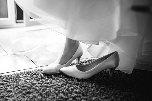 A greyscale of a bride in her wedding dress, wearing her shoes in preparation for the ceremony