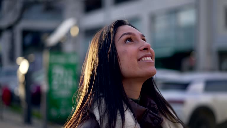 One hopeful young woman standing in street looking at sky with HOPE and FAITH. Happy female person in 20s stands in urban setting closeup face portrait