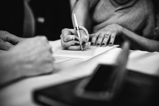 Ggreyscale image of a female signing a legal document with a pen in her hand A ggreyscale image of a female signing a legal document with a pen in her hand witness signature stock pictures, royalty-free photos & images