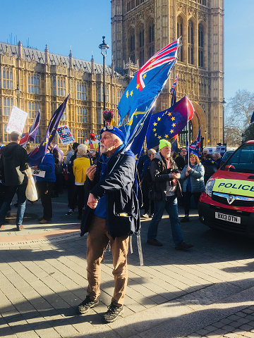 London, United Kingdom – February 14, 2019: In the foreground: a campaigner for  Brexit and People's Vote, in London, United Kingdom. In background: more campaigners, and Houses of Parliament.