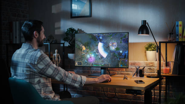 Young Man Playing a MMO RPG Video Game at Home on Desktop Computer . Male Gamer Competing for E.sports Championship. Loft Living Room in the Evening